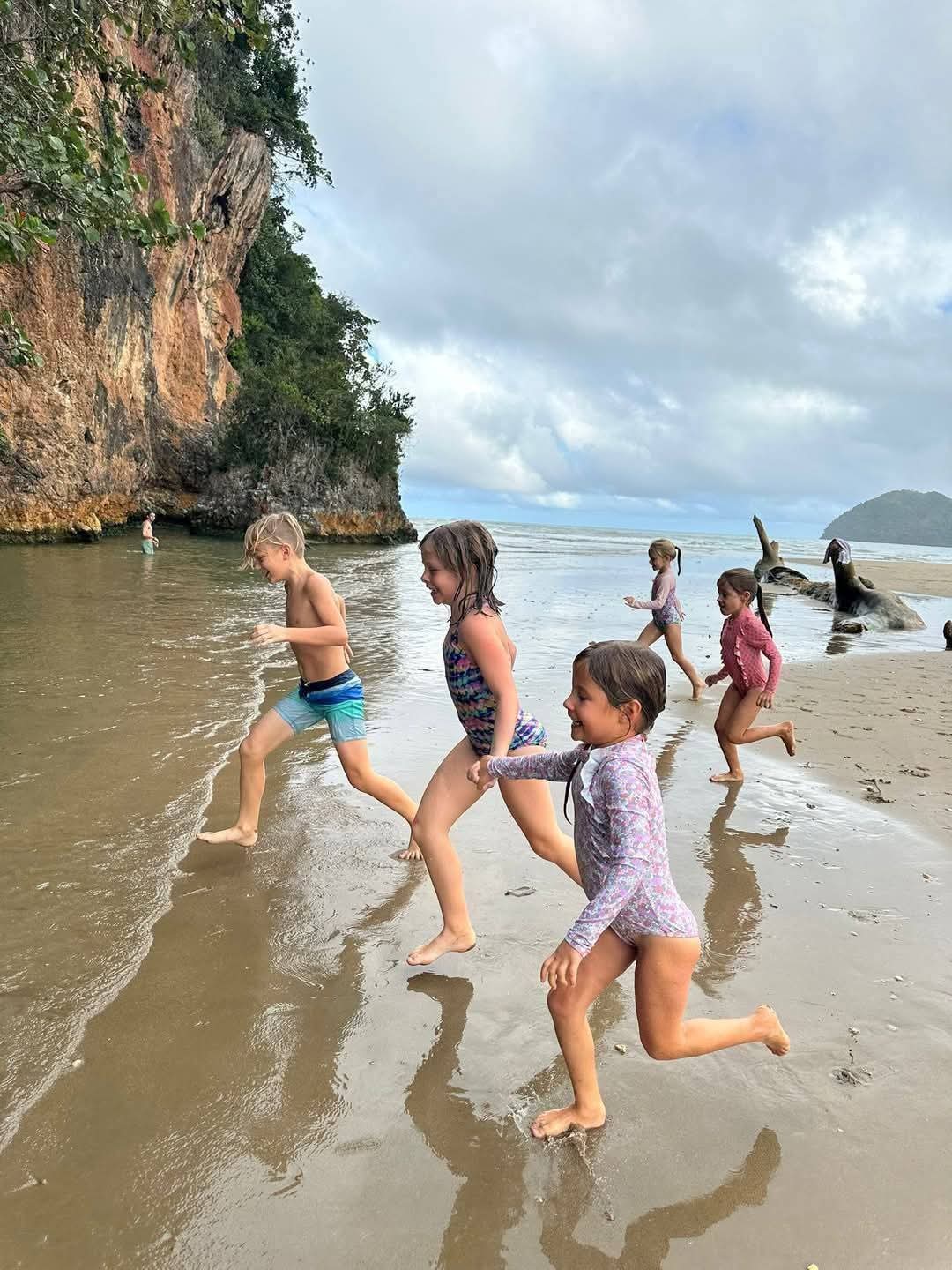 Children running along a Samaná beach beneath a jungle-covered cliff